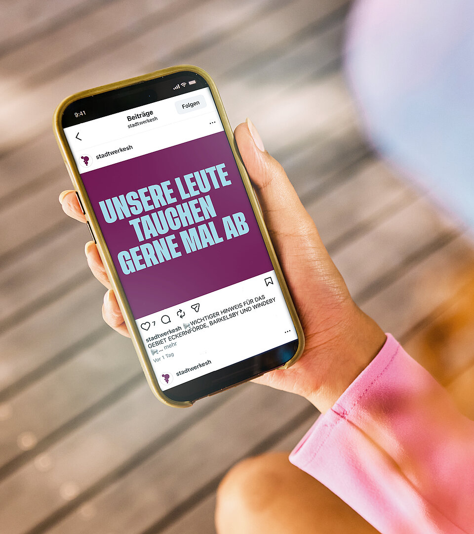 Person auf einem Holzsteg hält ein Mobiltelefon in der Hand mit geöffneter Werbeanzeige der Stadtwerke SH.