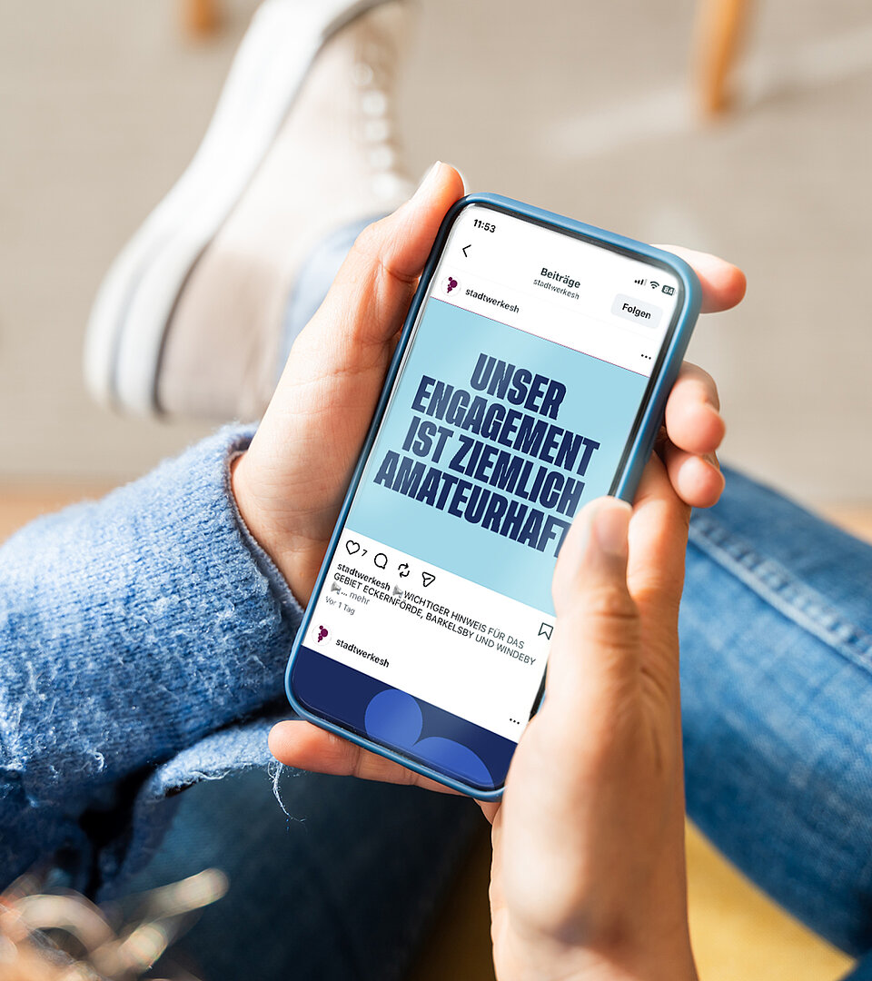 Person sitzt locker auf einem Stuhl und hält ein Mobiltelefon mit geöffneter Werbung der Stadtwerke SH in der Hand.