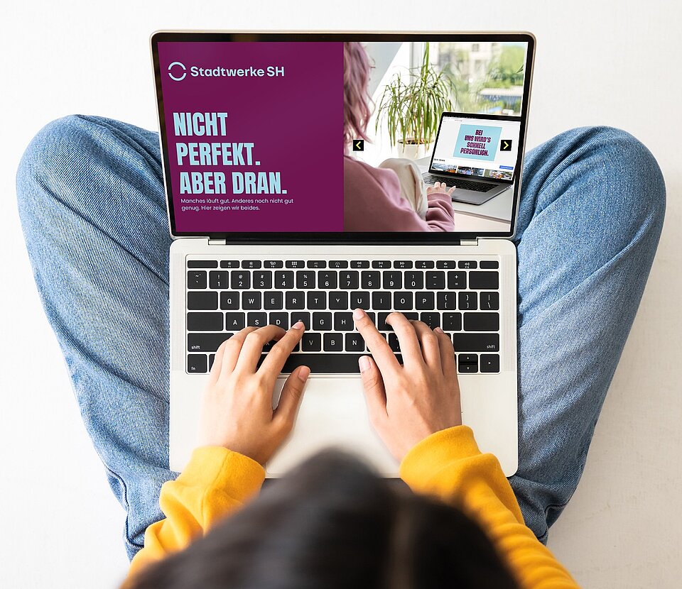 Person sitzt auf dem Boden und tippt in den Laptop ein bei geöffneter Stadtwerke SH Websiteansicht.