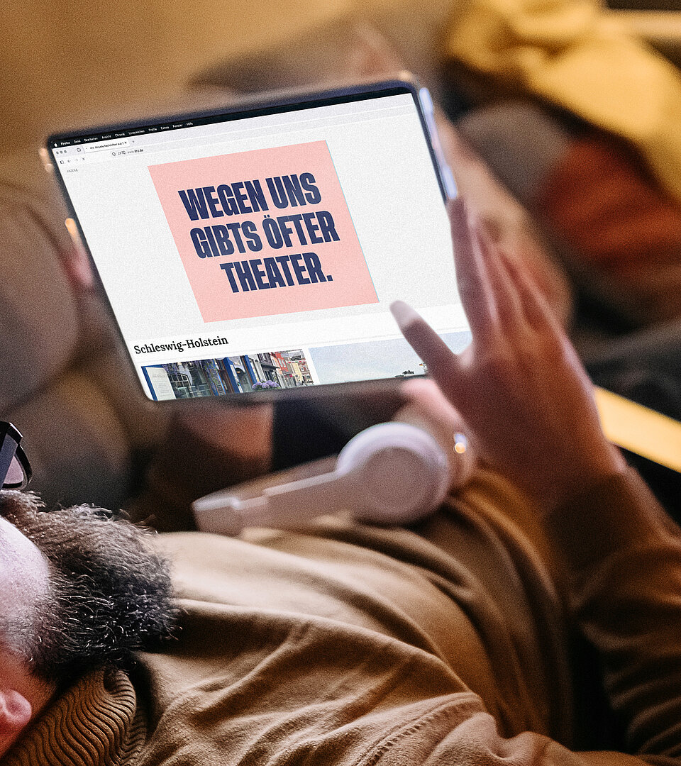 Person liegt auf einem Sofa und hält ein Tablet mit geöffneter Website und SH Werbung in der Hand.